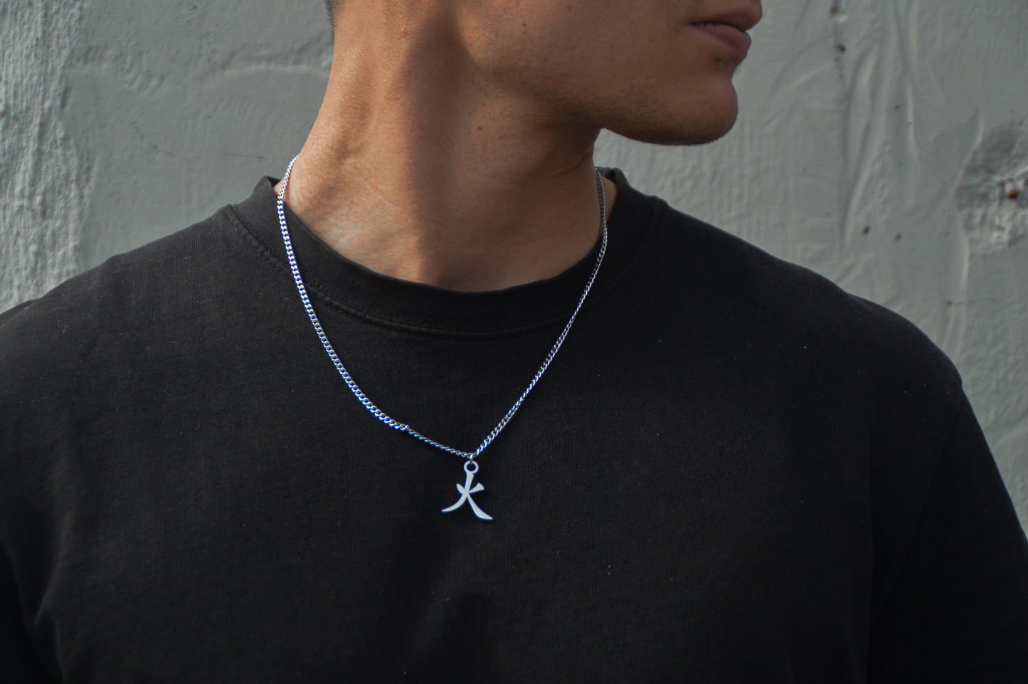 (火) Feuer Kanji Halskette aus der Godai Kollektion. Frontales Model Foto, mit schwarzem Tshirt und Blick zur Seite.