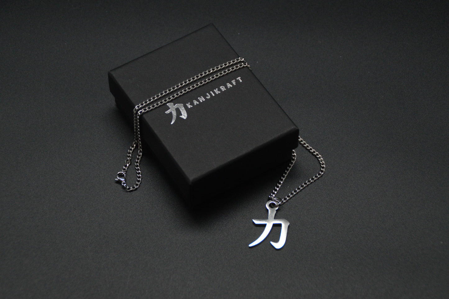 Das Japanische Schriftzeichen für Kraft als Edelstahlkette auf einem Schwarzen Hintergrund auf einer edlen KanjiKraft Geschenkbox. Das gleiche Kanji wie im Logo von KanjiKraft.