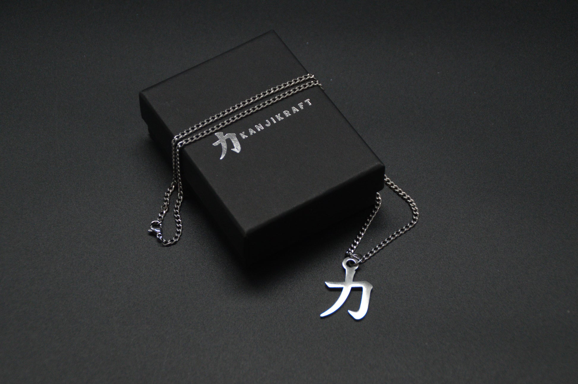 Das Japanische Schriftzeichen für Kraft als Edelstahlkette auf einem Schwarzen Hintergrund auf einer edlen KanjiKraft Geschenkbox. Das gleiche Kanji wie im Logo von KanjiKraft.