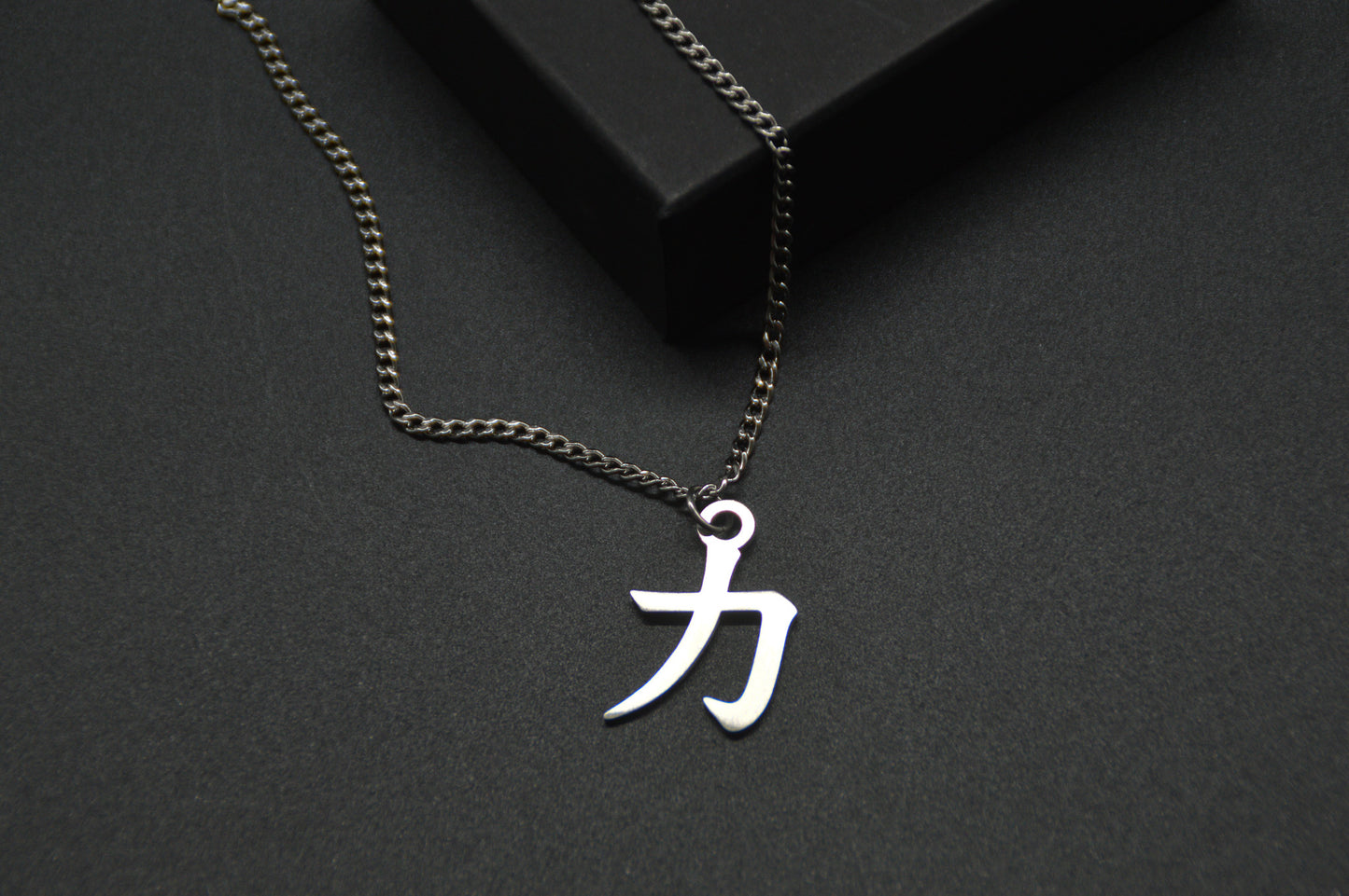Das Japanische Schriftzeichen für Kraft als Edelstahlkette auf einem Schwarzen Hintergrund im Close Up und leicht auf einer Kante liegend. Das gleiche Kanji wie im Logo von KanjiKraft,