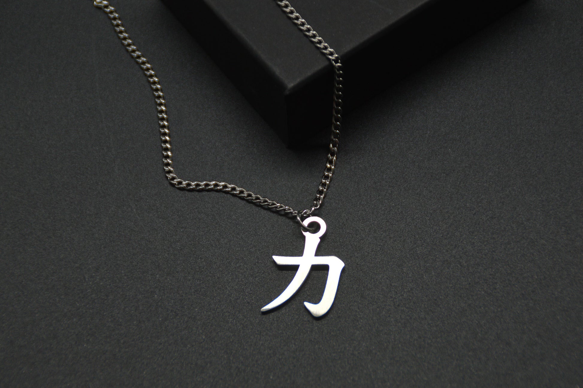 Das Japanische Schriftzeichen für Kraft als Edelstahlkette auf einem Schwarzen Hintergrund im Close Up und leicht auf einer Kante liegend. Das gleiche Kanji wie im Logo von KanjiKraft,