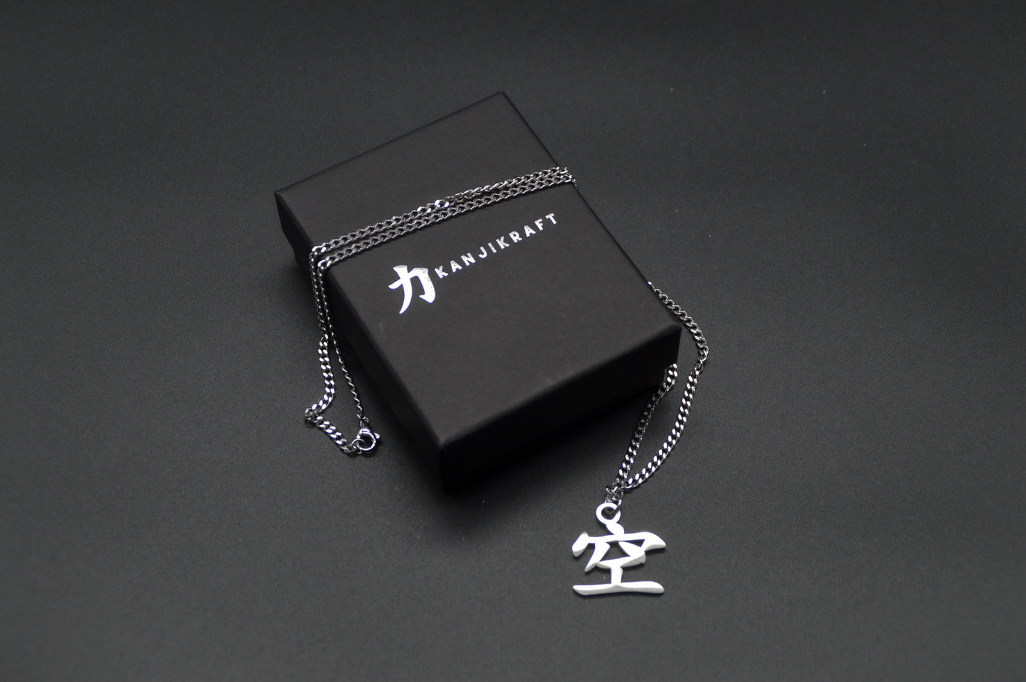 Leere Kanji Halskette aus der Godai Kollektion. Minimalistischer Japan Schmuck mit dem (空) Ku-Schriftzeichen als Edelstahl Anhänger liegt auf einer edlen KanjiKraft Geschenkbox
