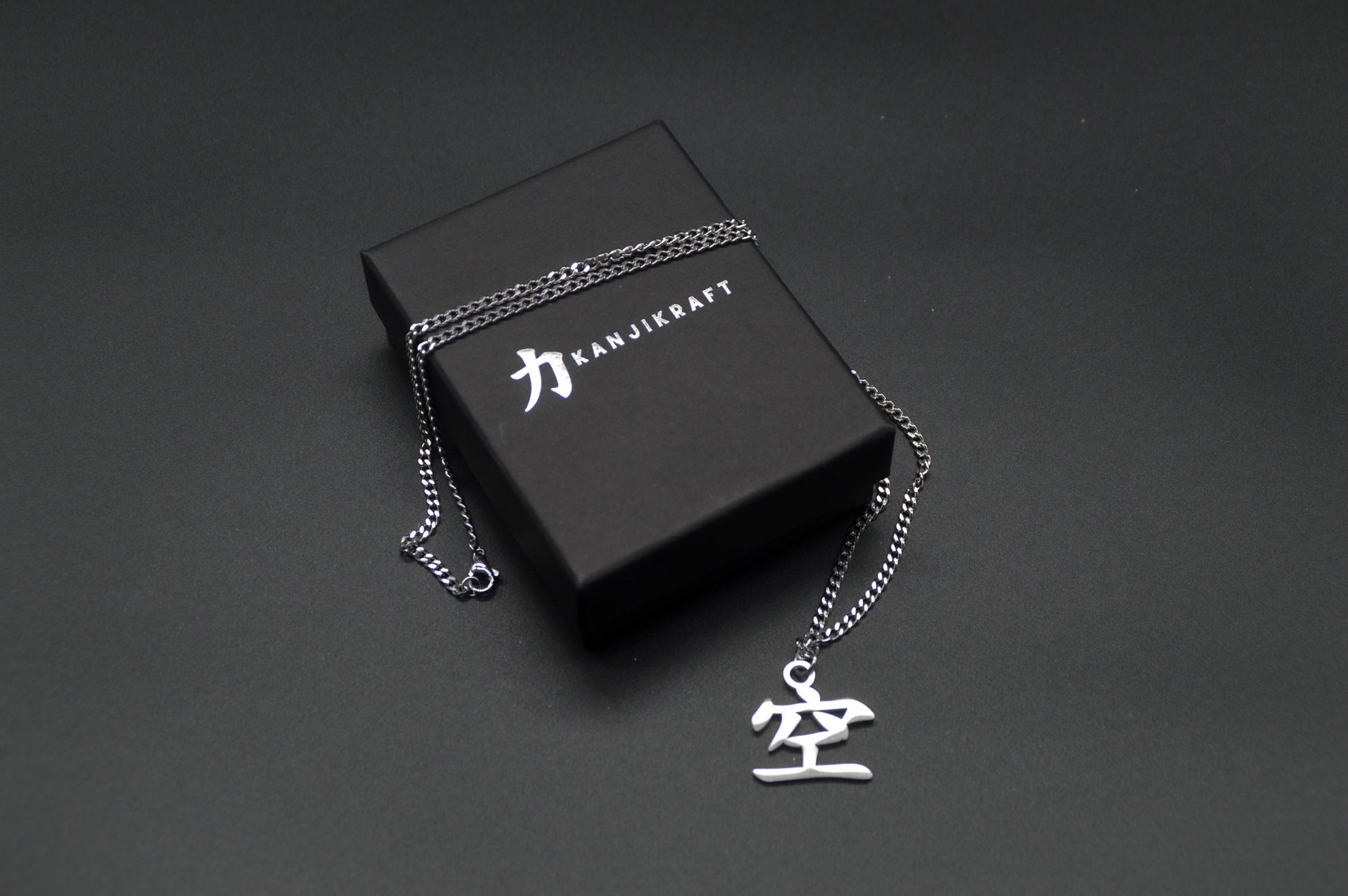 Leere Kanji Halskette aus der Godai Kollektion. Minimalistischer Japan Schmuck mit dem (空) Ku-Schriftzeichen als Edelstahl Anhänger liegt auf einer edlen KanjiKraft Geschenkbox