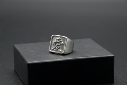 Das Japanische Schriftzeichen für Liebe auf einem Ring. Der Ring ist optisch ein Stempel Ring / Stamp Ring, wobei das Kanji 愛 drauf ist. Zu sehen ist der weiße Ring auf einem kleinen Podest von unserer KanjiKraft Box.