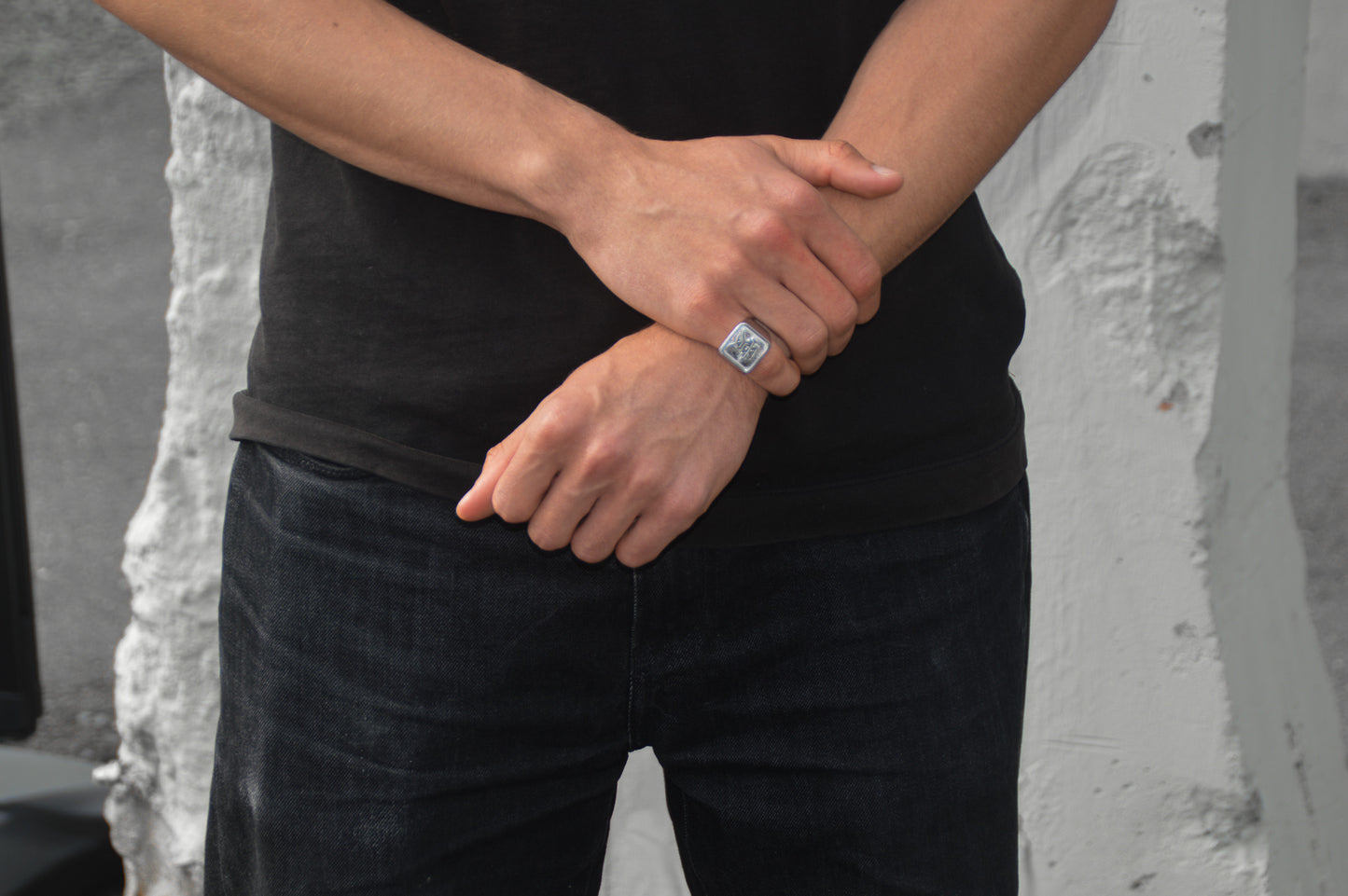 Das Japanische Schriftzeichen für Liebe auf einem Ring. Der Ring ist optisch ein Stempel Ring / Stamp Ring, wobei das Kanji 愛 drauf ist. Zu sehen ist der Weiße Ring getragen an der rechten Hand auf dem kleinen Finger während der Rechte Arm den linken Arm greift. Frontales Foto