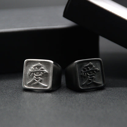 Das Japanische Schriftzeichen für Liebe auf einem Ring. Der Ring ist optisch ein Stempel Ring / Stamp Ring, wobei das Kanji 愛 drauf ist. Beide Ringe sind aus Edelstahl und der linke Ring ist in silberner Farbe und der rechte ist Schwarz und hat eine schwarze Beschichtung.