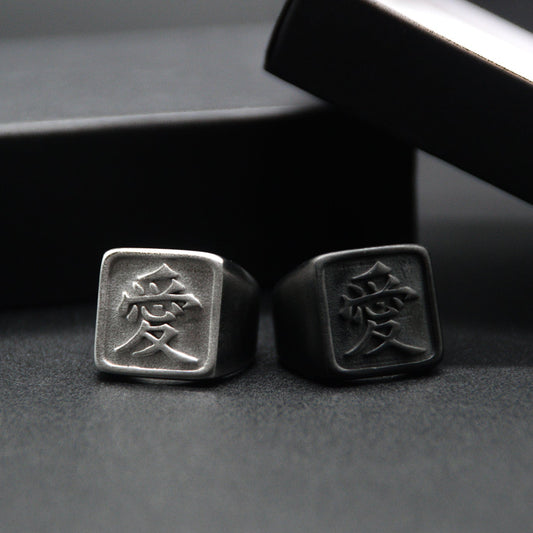 Das Japanische Schriftzeichen für Liebe auf einem Ring. Der Ring ist optisch ein Stempel Ring / Stamp Ring, wobei das Kanji 愛 drauf ist. Beide Ringe sind aus Edelstahl und der linke Ring ist in silberner Farbe und der rechte ist Schwarz und hat eine schwarze Beschichtung.