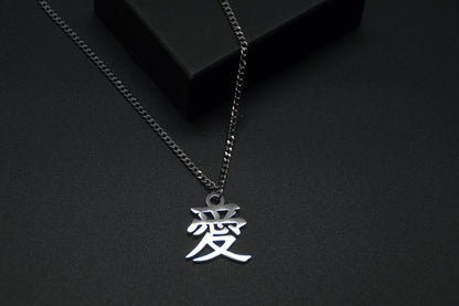 Das Japanische Schriftzeichen (Kanji für Liebe). Edelstahl Halskette mit dem Schriftzeichen 愛 als Anhänger auf einem Schwarzen Hintergrund als Nahaufnahme. Die Kette liegt leicht auf einer Kante an.