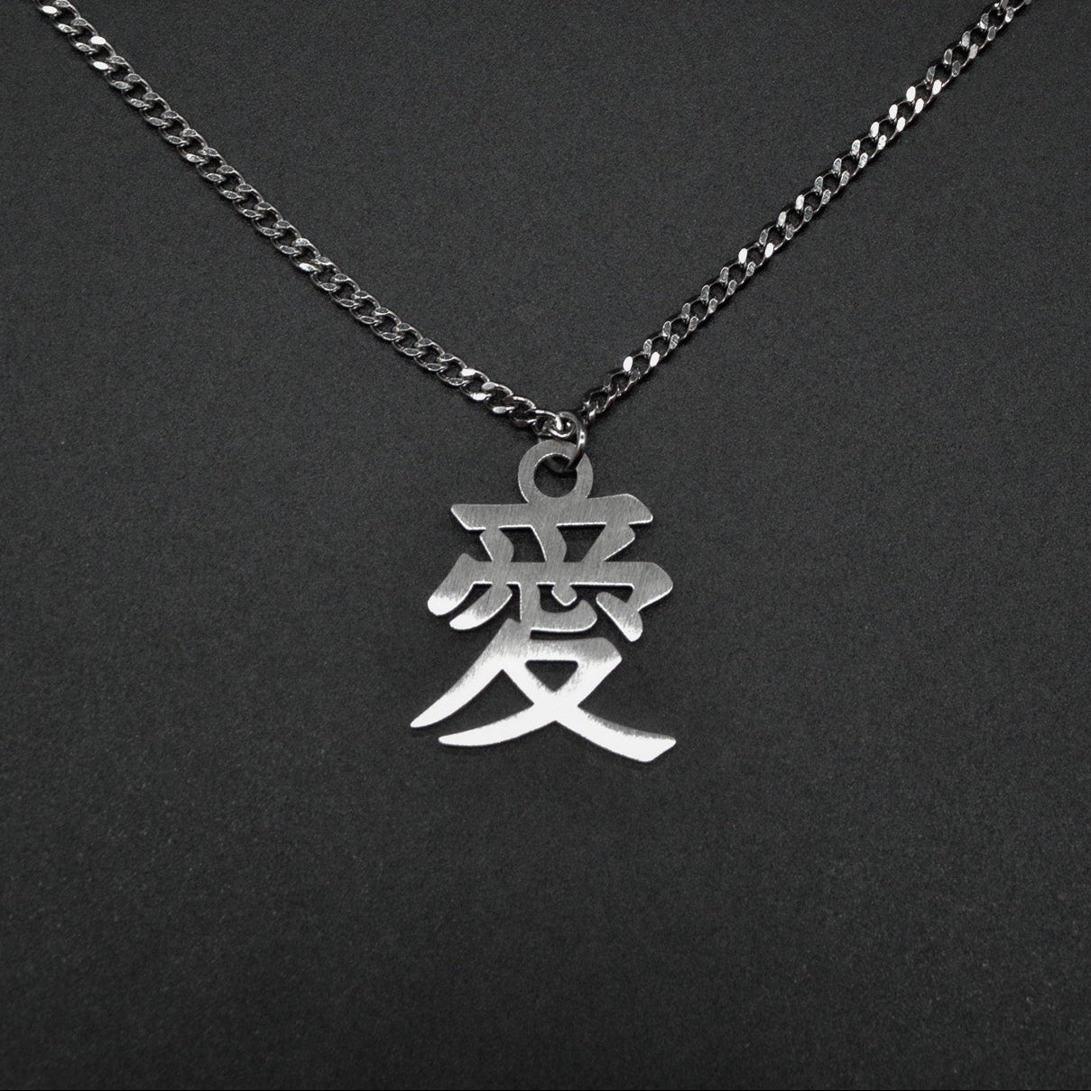 Das Japanische Schriftzeichen (Kanji für Liebe). Edelstahl Halskette mit dem Schriftzeichen 愛 als Anhänger auf einem Schwarzen Hintergrund als Nahaufnahme.