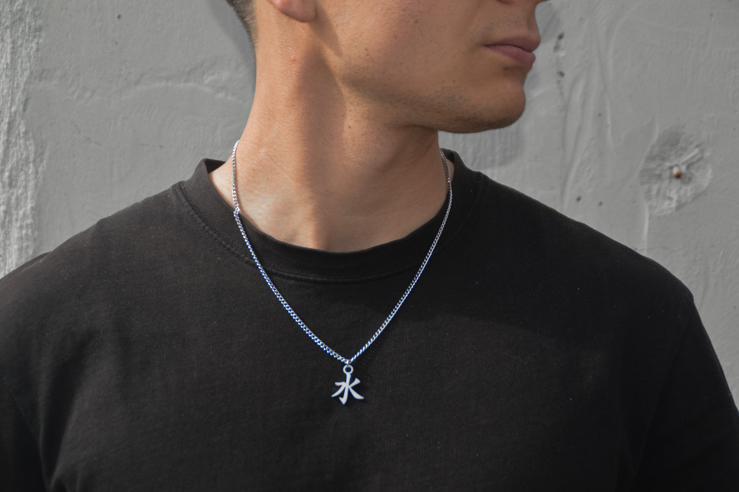 (水) Wasser Kanji Halskette aus der Godai Kollektion. Frontales Model Foto, mit schwarzem Tshirt und Blick zur Seite.