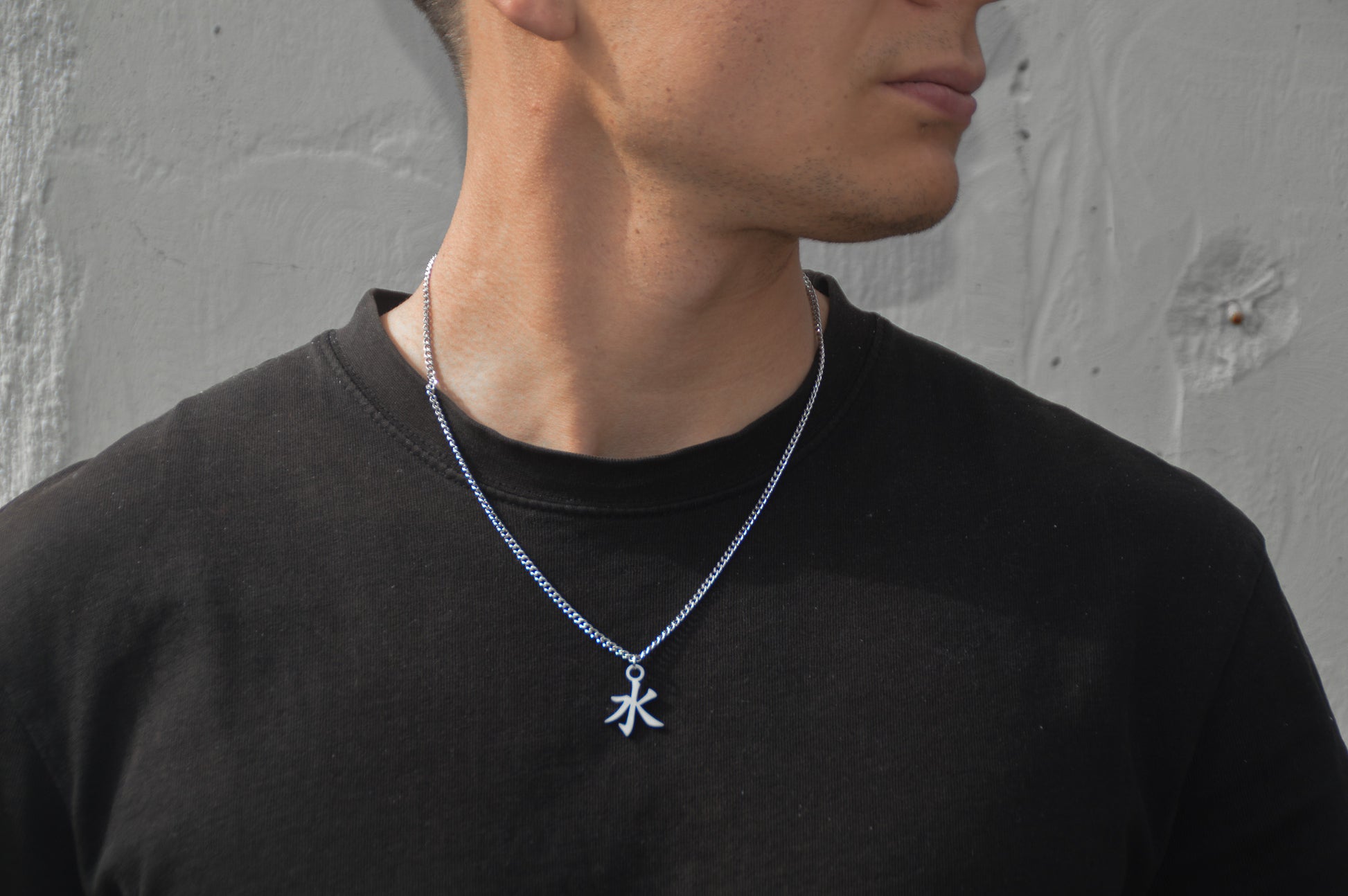(水) Wasser Kanji Halskette aus der Godai Kollektion. Frontales Model Foto, mit schwarzem Tshirt und Blick zur Seite.
