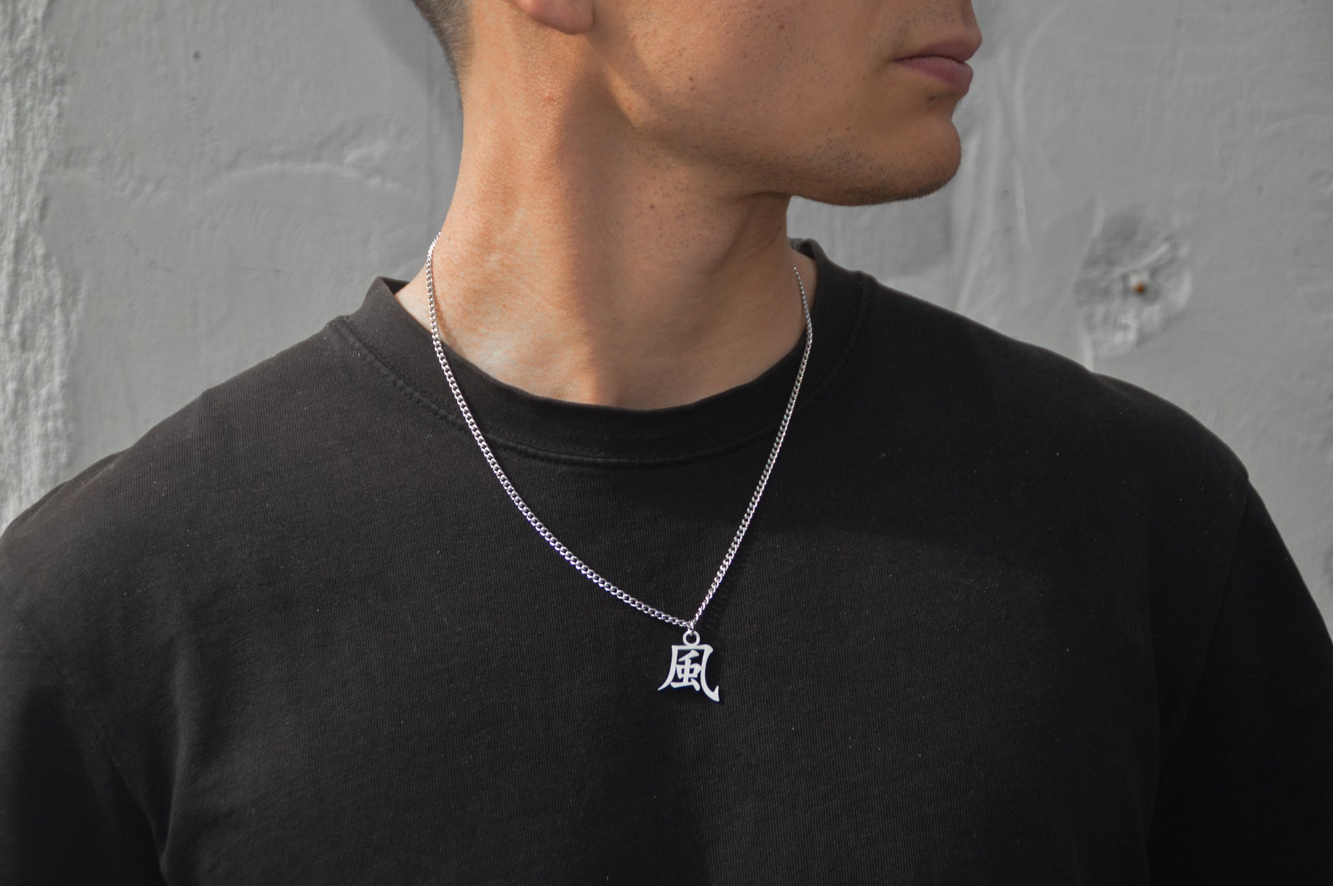 (風) Wind Kanji Halskette aus der Godai Kollektion. Frontales Model Foto, mit schwarzem Tshirt und Blick zur Seite.